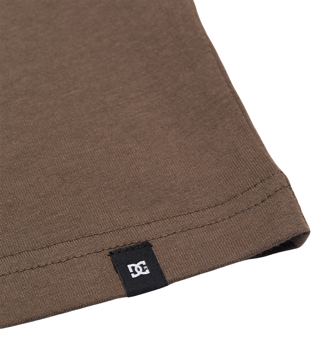 Close-up of the hem on the Men's DC Star Tee by DC Shoes, a relaxed fit brown shirt featuring a small black tag with the white DC logo sewn into the edge.