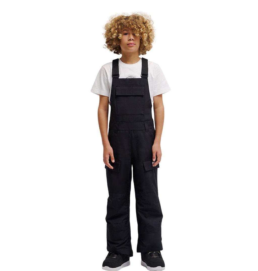A person with curly blond hair wearing a white t-shirt under the DC Shoes Roadblock Youth Bib and black shoes stands facing forward against a plain white background.