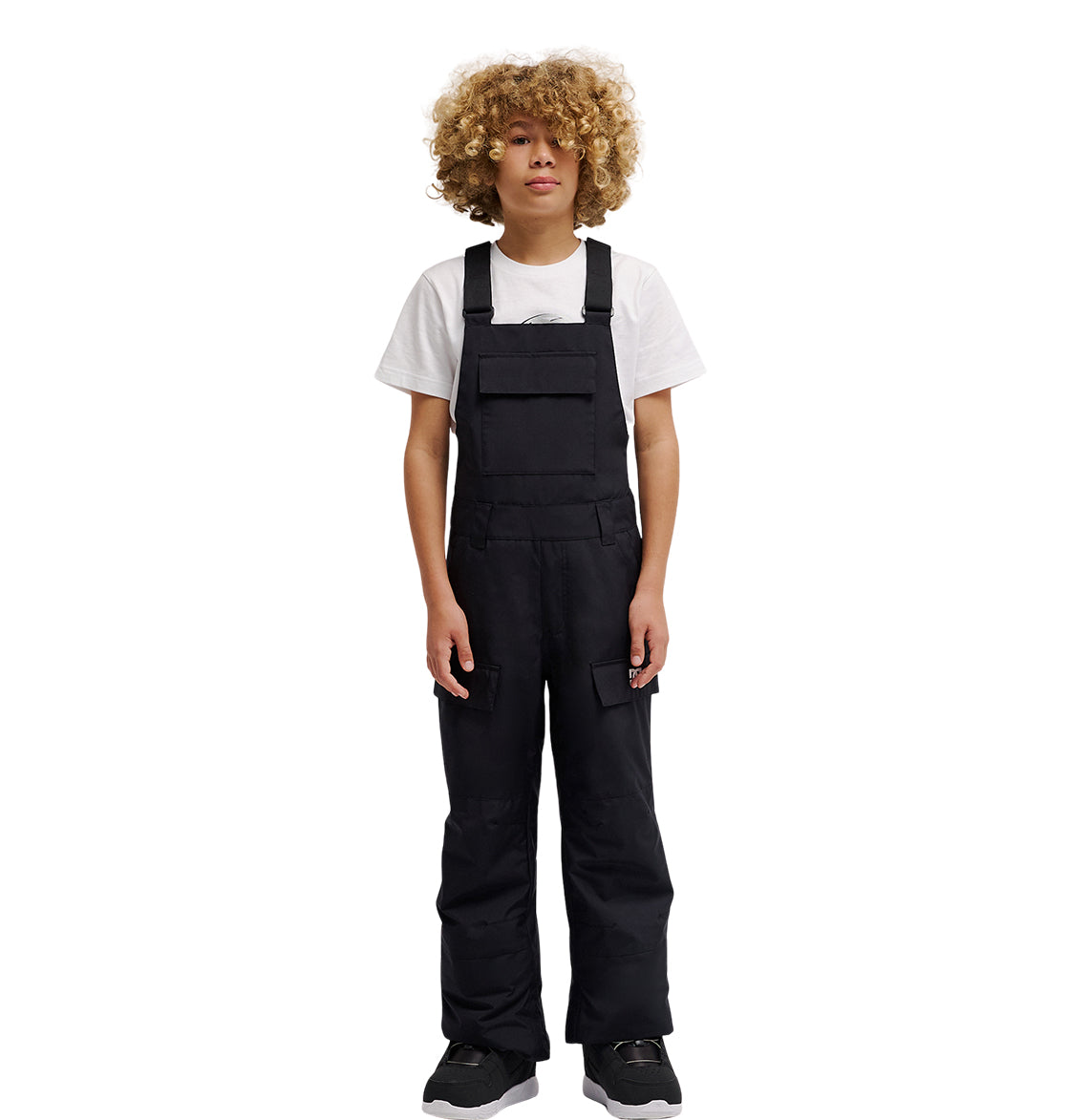 A person with curly blond hair wearing a white t-shirt under the DC Shoes Roadblock Youth Bib and black shoes stands facing forward against a plain white background.