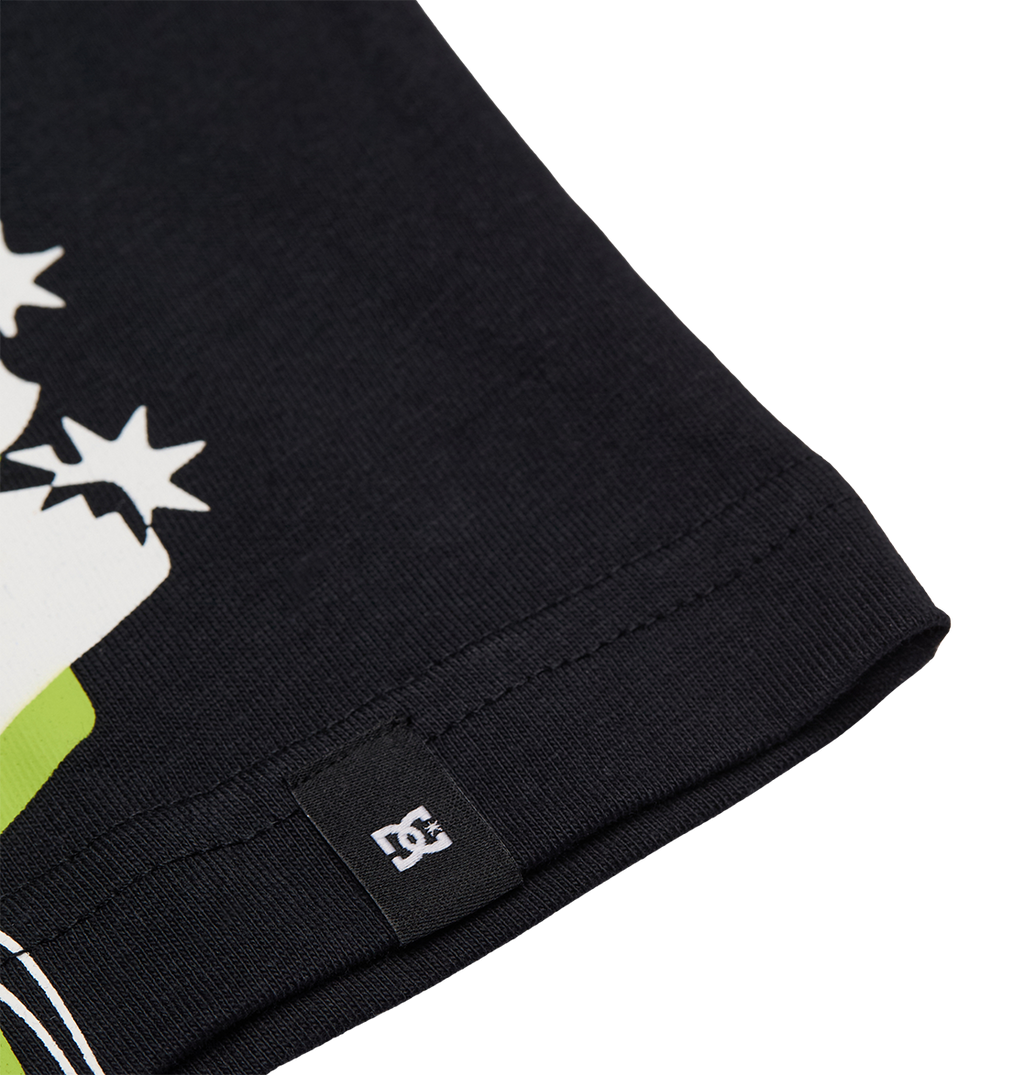 Close-up of the black fabric edge of the DC Side Flame Tee Youth by DC Shoes, featuring a small stitched tag with a white DC logo. Partially visible on the fabric are colorful graphic elements and some white star shapes from the skate tee’s design.