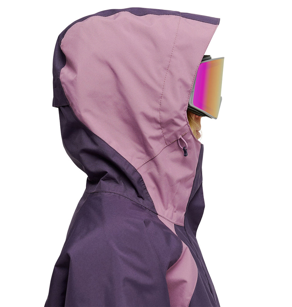 Model in the DC Shoes Everfrost Jacket, a two-toned purple and pink insulated style with a hood, paired with reflective ski goggles. Side profile view on a white background.