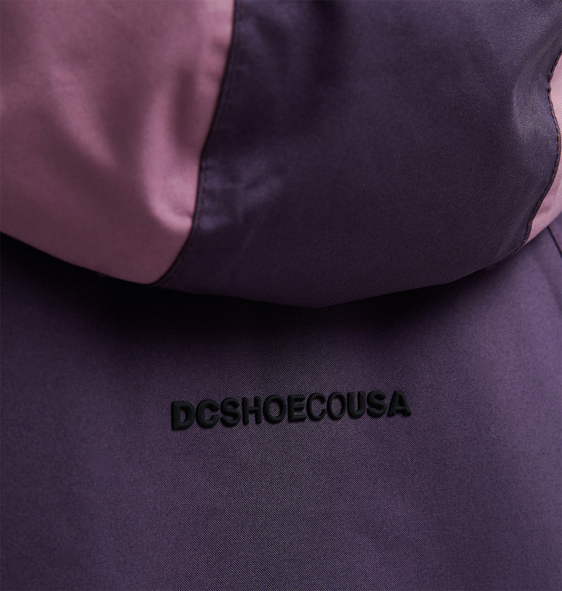 Close-up of the DC Shoes Everfrost Jacket in purple and pink, featuring the embroidered text DCSHOECOUSA on the fabric.