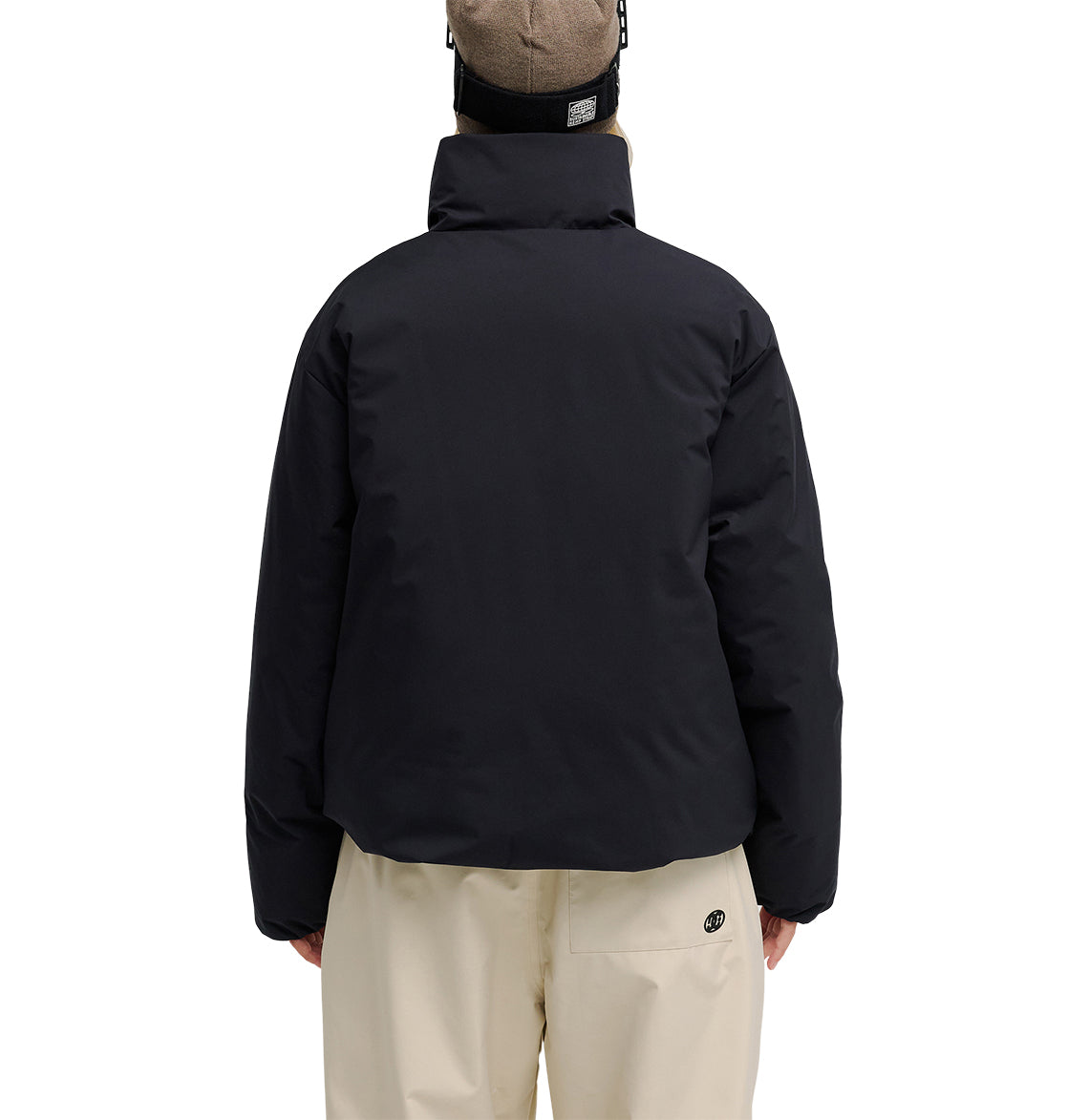 A person is facing away, wearing the DC Shoes Aura Puffer Jacket in black, paired with beige pants and a beige beanie. The plain white background highlights the outfit from the back.