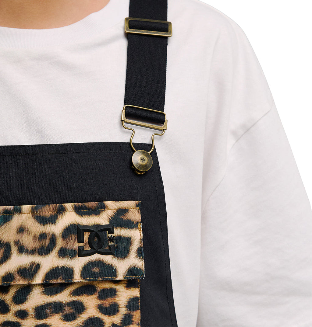 A person wears DC Shoes’ Valiant Bib Pants, featuring black overalls with a leopard print chest pocket displaying the DC logo and paired with a white shirt, offering breathable protection. Only the chest and strap area are visible against a white background.