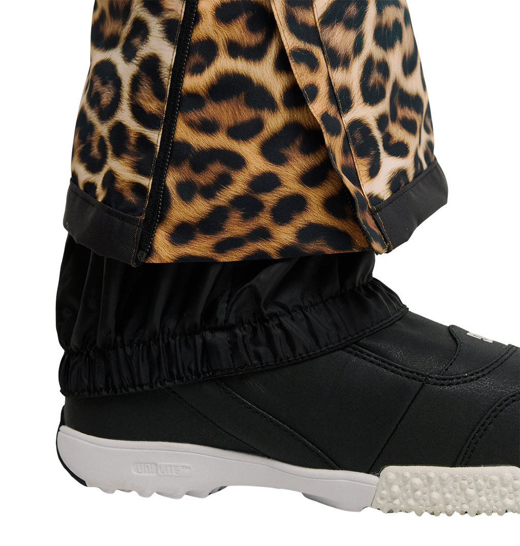 Close-up of a person’s lower leg wearing DC Shoes Valiant Bib Pants in leopard print, paired with black elastic gaiters layered over a black shoe with a white textured sole, offering breathable protection for enhanced snow performance.