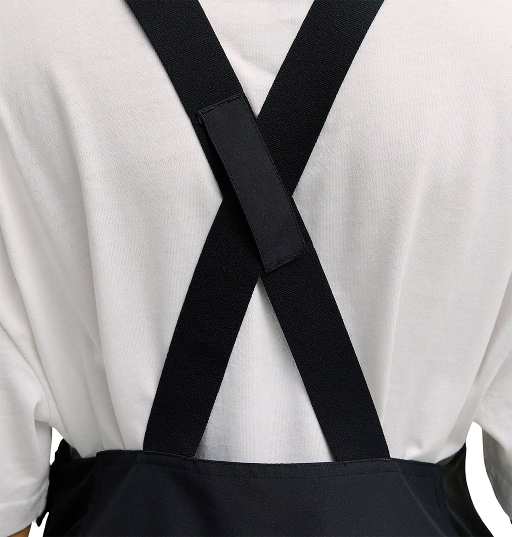 A close-up of a person wearing the DC Shoes Valiant Bib Pants, featuring crossed straps on their back and designed for breathable protection throughout the workday.
