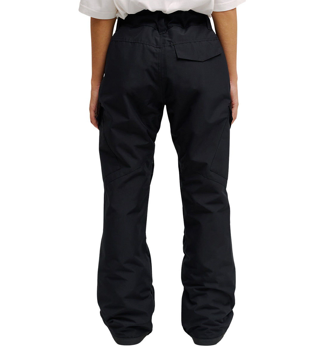 A person is standing with their back to the camera, wearing DC Shoes’ Nonchalant Pant—a pair of black, loose-fitting insulated pants featuring a flap pocket on the right side and engineered for optimal snow performance—paired with a white shirt.