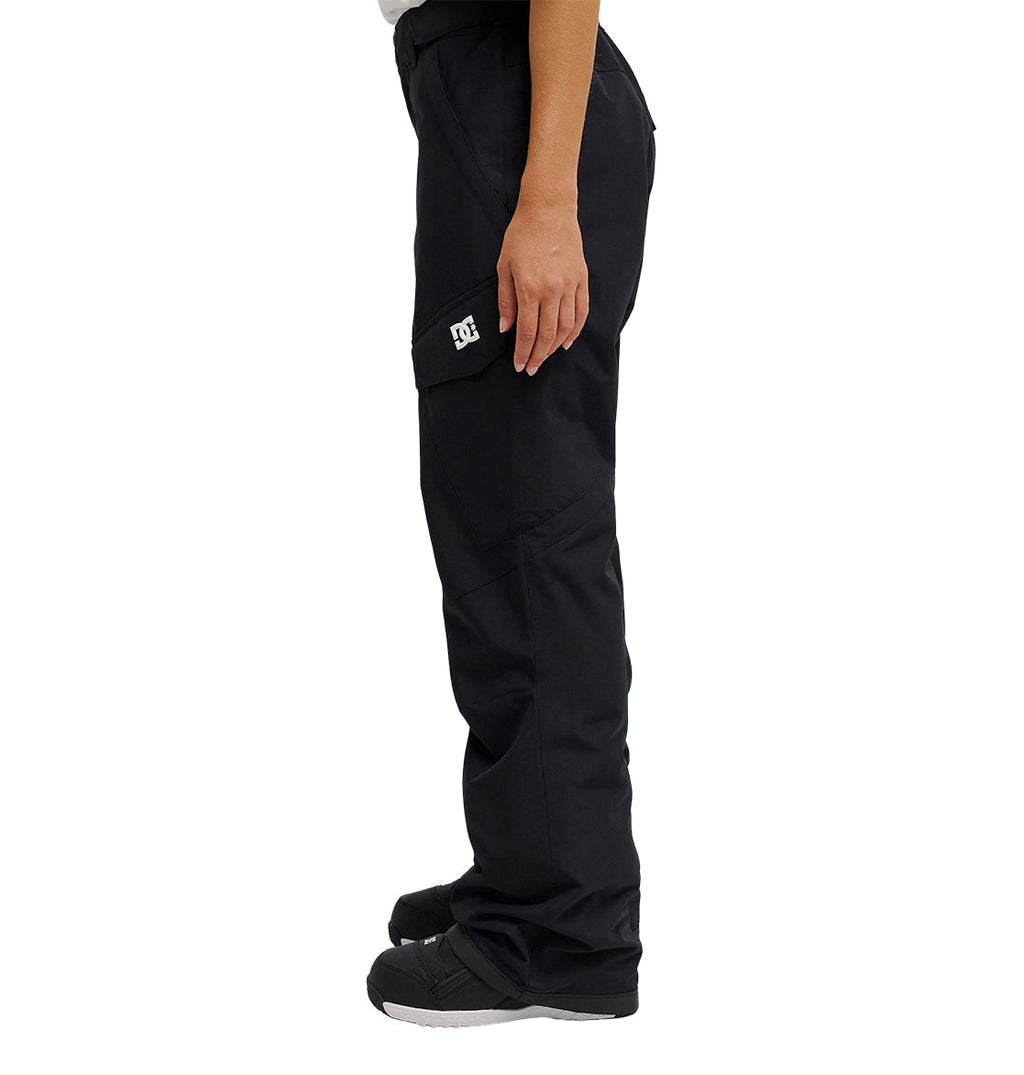A person is standing in profile view against a white background, wearing the DC Shoes Nonchalant Pant—black, waterproof insulated cargo pants with a DC logo on the pocket—and black and white shoes.