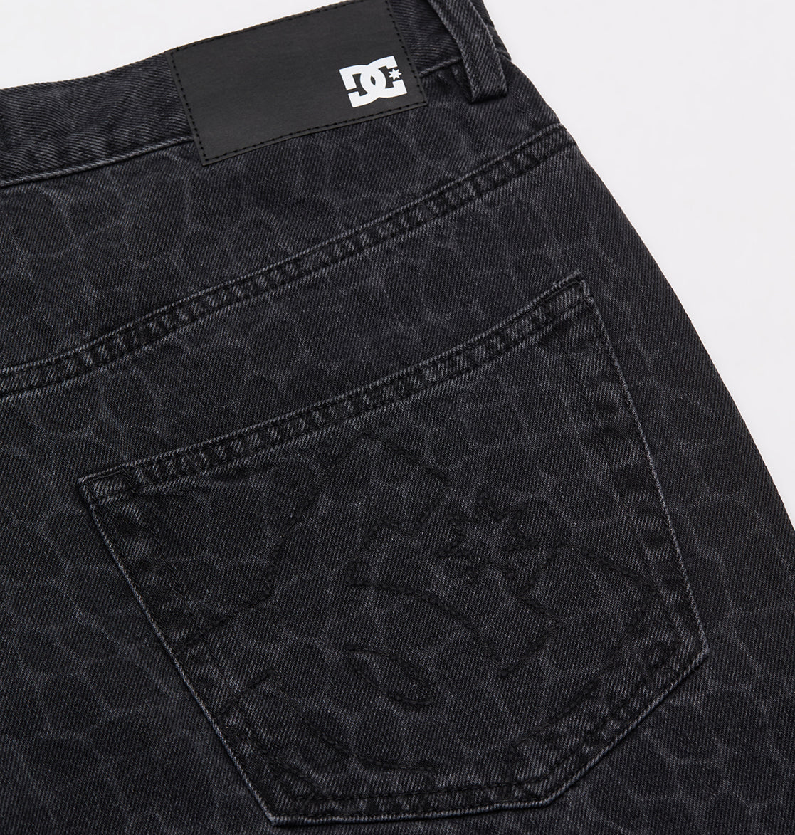 Close-up of the Men's Baggy Denim Snake Print Pant by DC Shoes, showing the black snake print pattern on the back pocket and a small black and white DC Shoes logo tag near the waistband.
