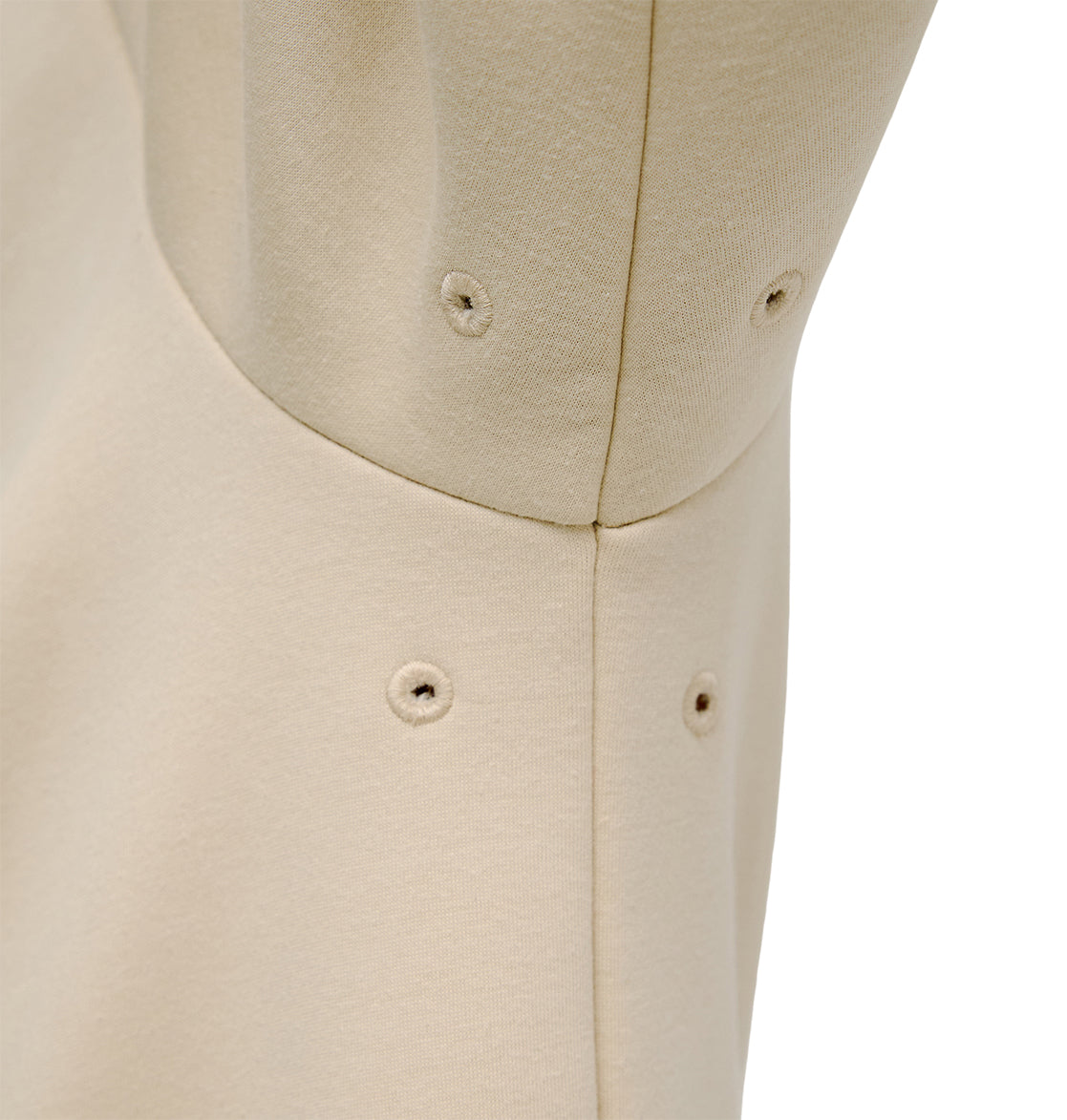 Close-up of the beige fabric on the DC Shoes Snowstar, featuring visible stitching and four small metal eyelets arranged in a pattern—details that contribute to a comfortable fit and enhanced weather protection, likely as part of this outerwear garment.