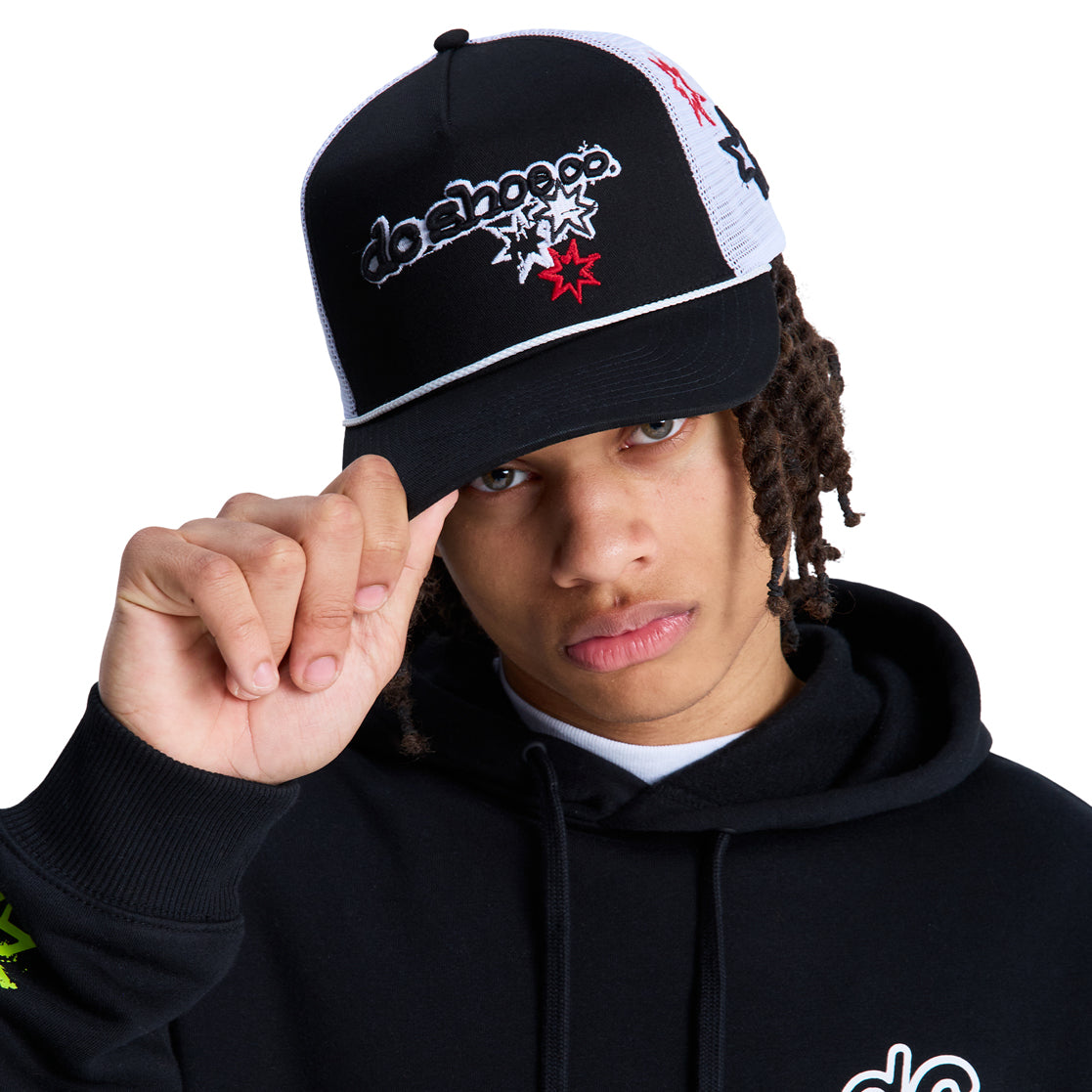 A person wearing a black hoodie and a Reebok Side Star Trucker hat with embroidered designs lifts the hat's brim, looking directly at the camera against a white background.