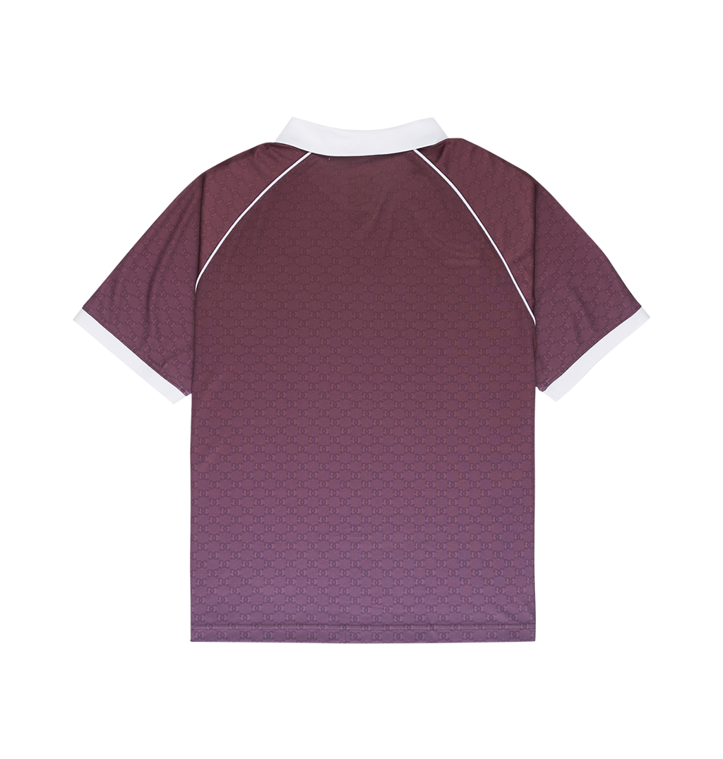 A person with short, braided hair is seen from behind in the DC Shoes Men's DC Soccer Top—a maroon skate-inspired jersey with a white collar and sleeve trim—paired with light blue jeans against a plain white background.