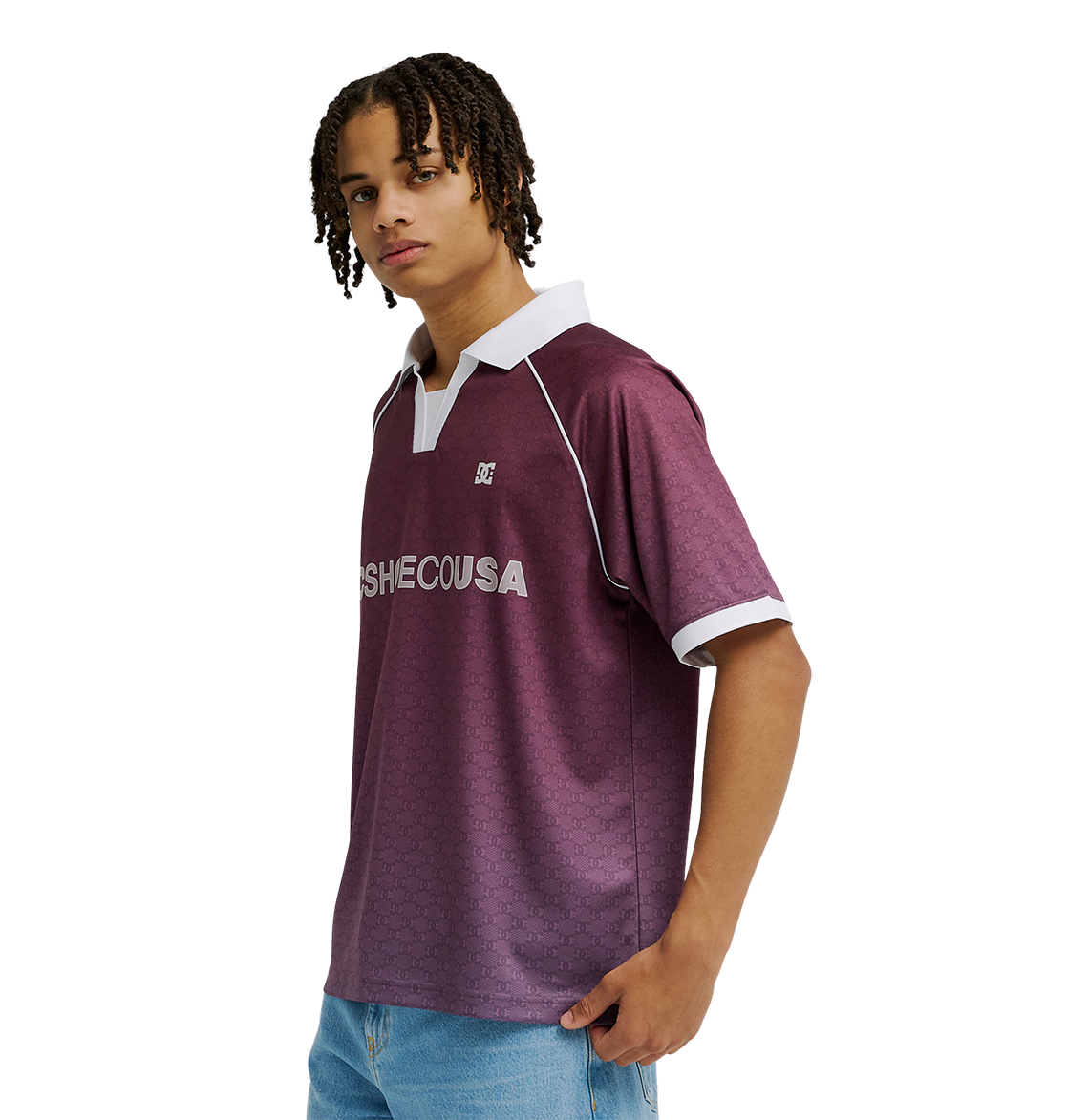 A man with short, curly hair wears the Men's DC Soccer Top by DC Shoes—a maroon polo with white collar and sleeve trim, athletic styling, and breathable fabric—paired with light blue jeans, standing against a plain white background.