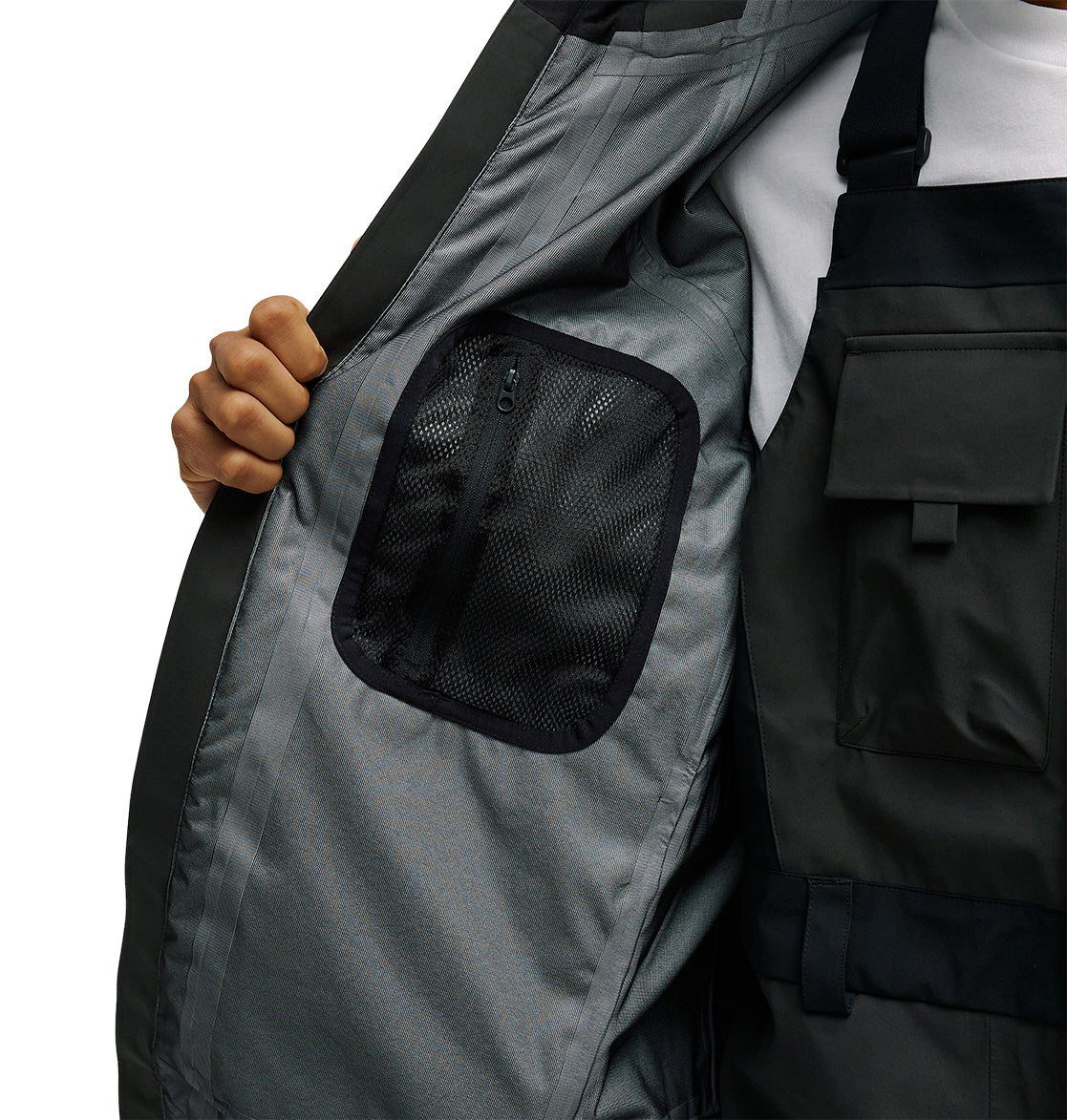 A person opens the DC Shoes Storm Divison 3L Jacket 30K, revealing a mesh zippered pocket on the inner lining to showcase its storage details.