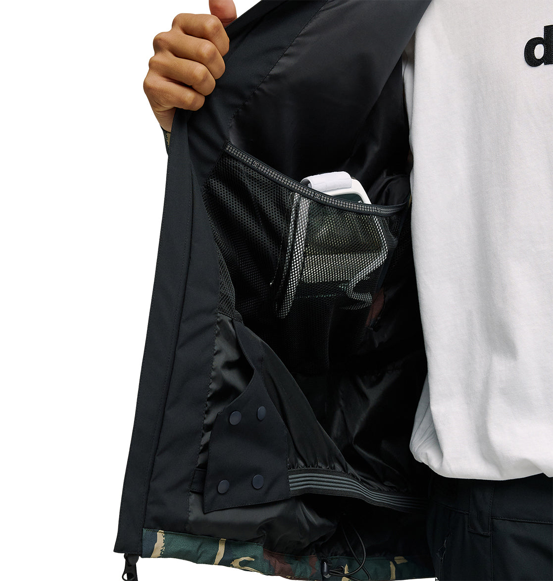 A person opens the black DC Shoes Edge Jacket 20K to reveal a mesh inner pocket holding a white object. They are wearing a white shirt and black pants.