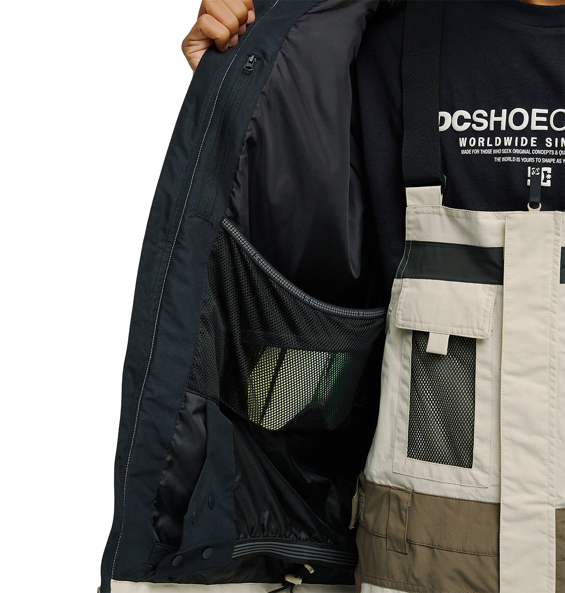 A person opens a DC Shoes Mountain Lab Jacket 20K, revealing the inner mesh pocket and emphasizing the jacket’s breathable protection and snow-ready performance. Underneath, they’re wearing a black DC Shoes Worldwide t-shirt. Only their torso and part of one hand are visible.