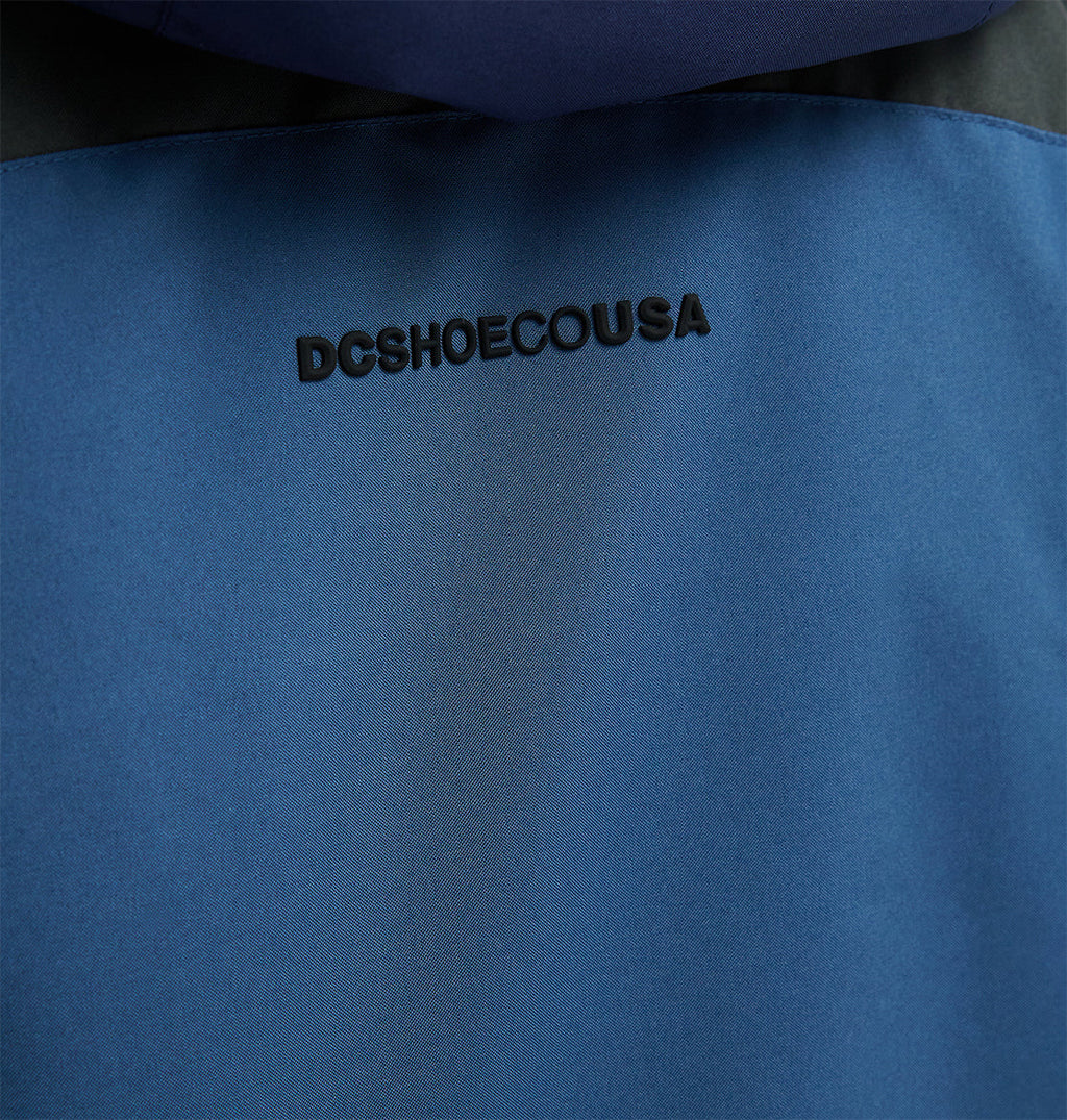 Close-up of a blue Coldsmoke Jacket 10K by DC Shoes, featuring “DCSHOESCOUSA” embroidered in black letters near the top center, highlighting its breathable protection designed for optimal snow performance.