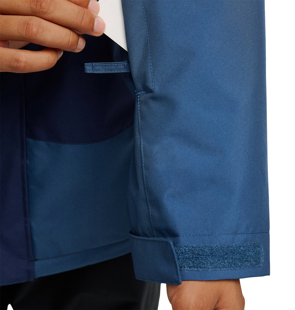 A person adjusts the Velcro cuff of a blue DC Shoes Coldsmoke Jacket 10K sleeve while holding a white object in their other hand, ensuring optimal waterproofing and breathable protection for enhanced comfort in challenging conditions.