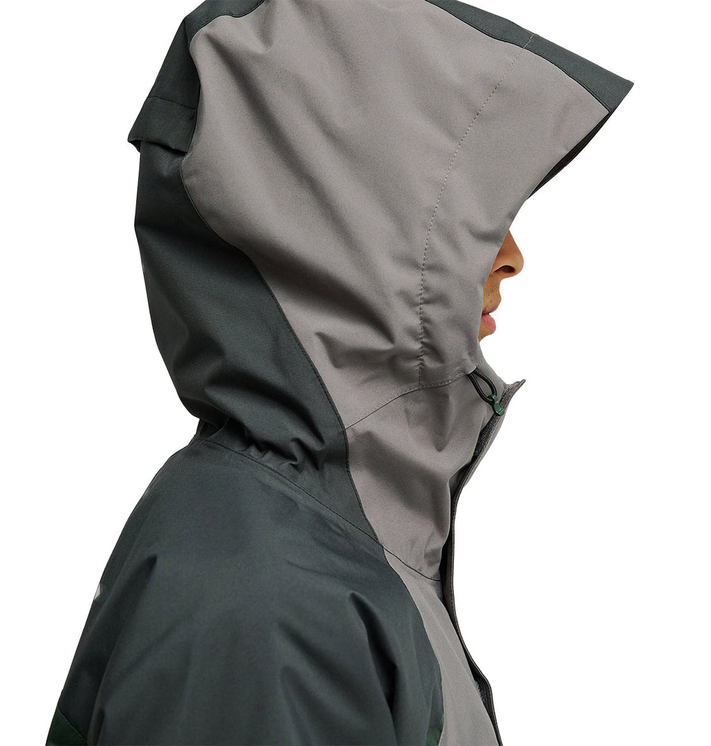 A person wearing the DC Shoes Coldsmoke Jacket 10K in gray stands in profile against a plain background. The jacket’s hood is up, covering most of the head and offering breathable protection, leaving only part of the face visible.