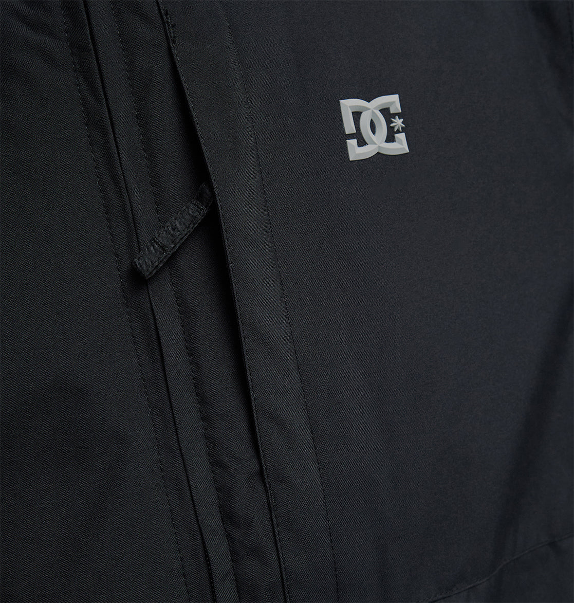 Close-up of the DC Shoes Basis Jacket 10K in black, showcasing a small white DC Shoes logo on the chest, with detailed pocket accents and visible stitching.