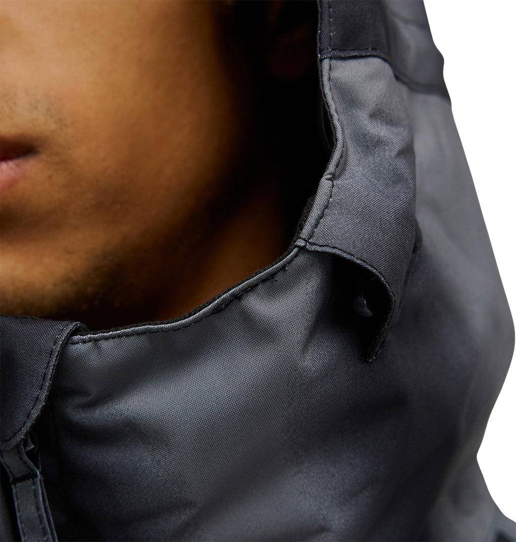 Close-up of a person wearing the DC Shoes Basis Jacket 10K in dark gray, with the hood up, showing part of their face and the textured fabric of the hood. The background is plain white.