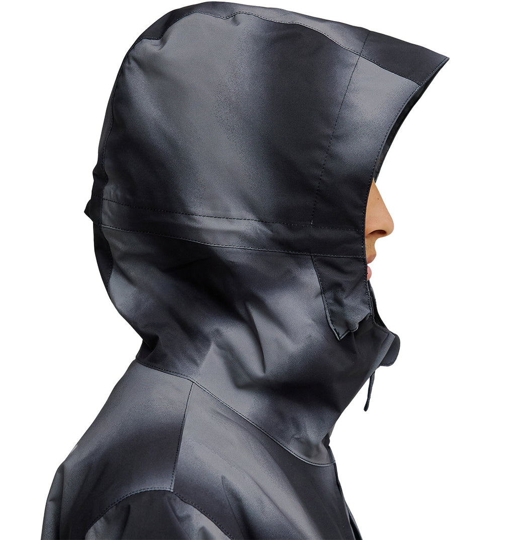 A person in profile view wears the DC Shoes Basis Jacket 10K—a shiny, dark gray waterproof jacket with the hood up, covering most of their head and face. The background is plain white.