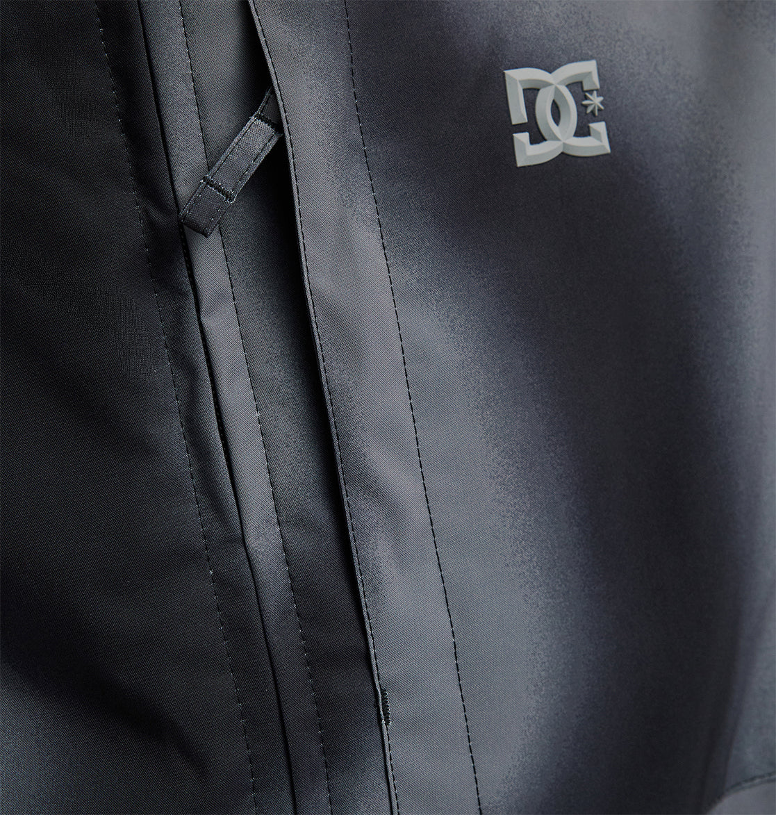 Close-up of the DC Shoes Basis Jacket 10K, a black insulated ski jacket featuring a front pocket with a flap and the white DC Shoes logo printed on the chest.