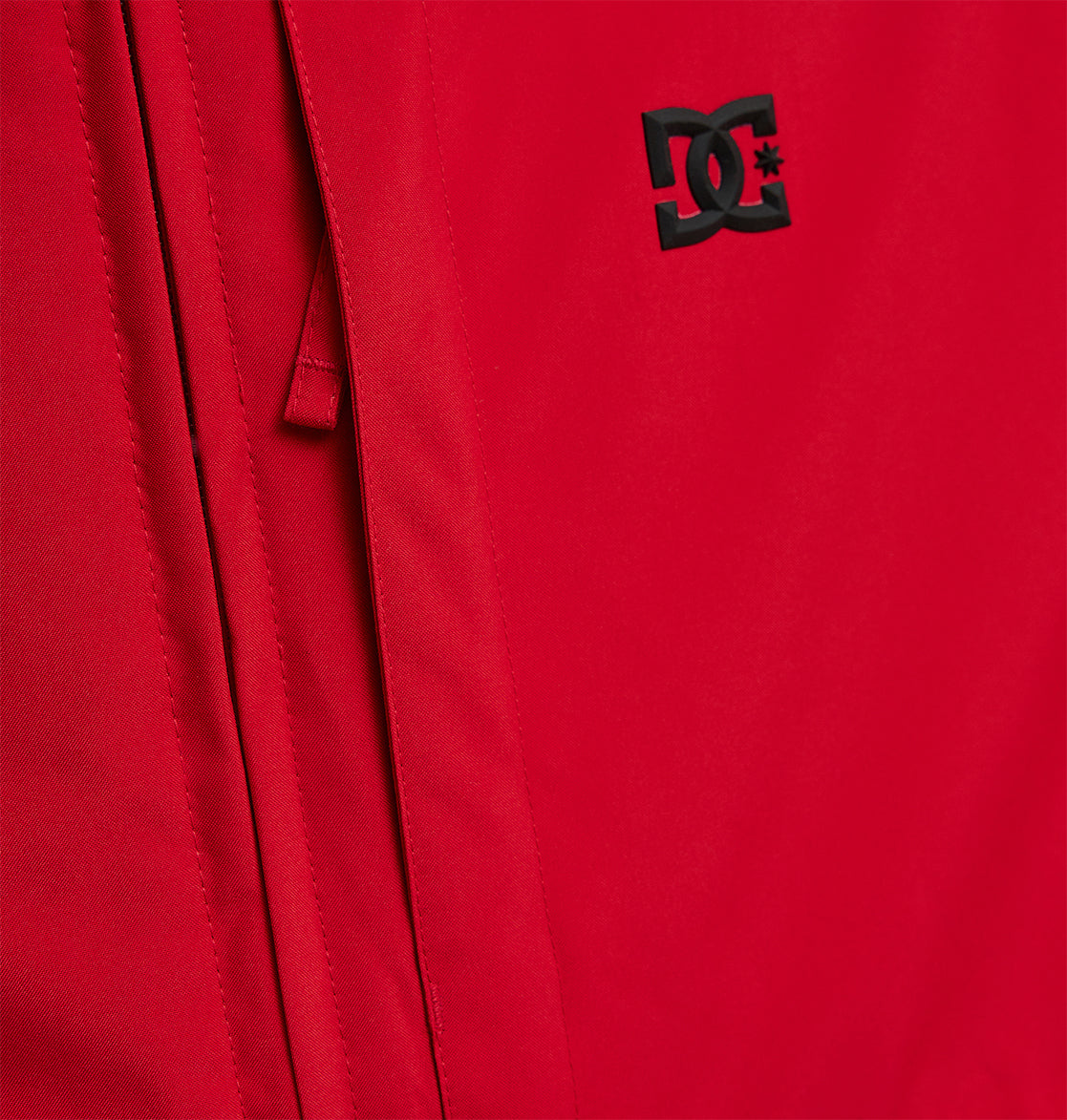 Close-up of the Basis Jacket 10K by DC Shoes, a red insulated jacket showcasing a black DC Shoes logo with a partially visible zipper along the left side.