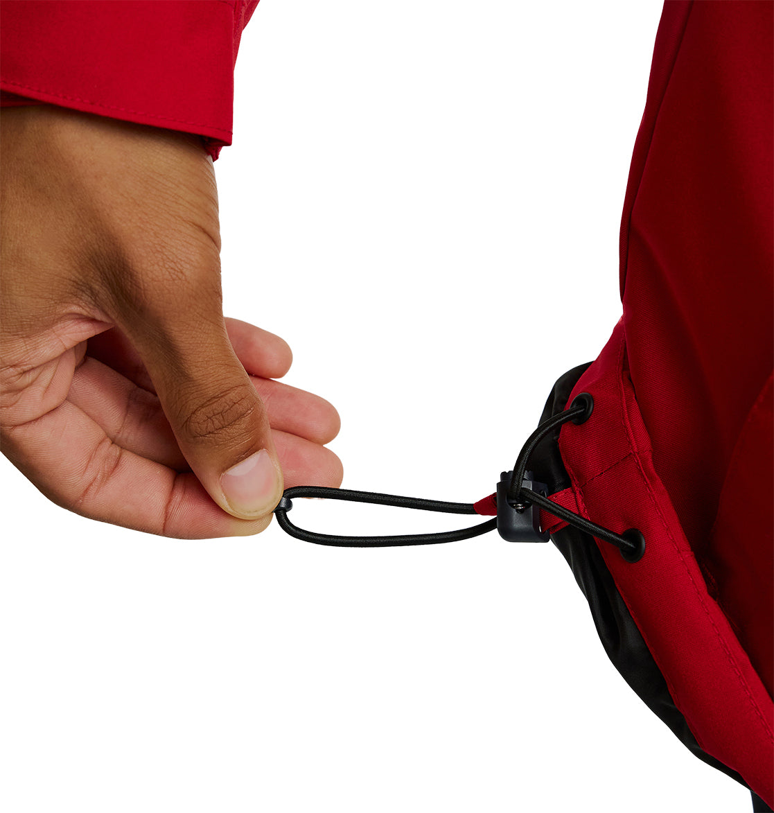 A hand pulls the adjustable drawstring cord at the hem of a red DC Shoes Basis Jacket 10K, tightening the fit.