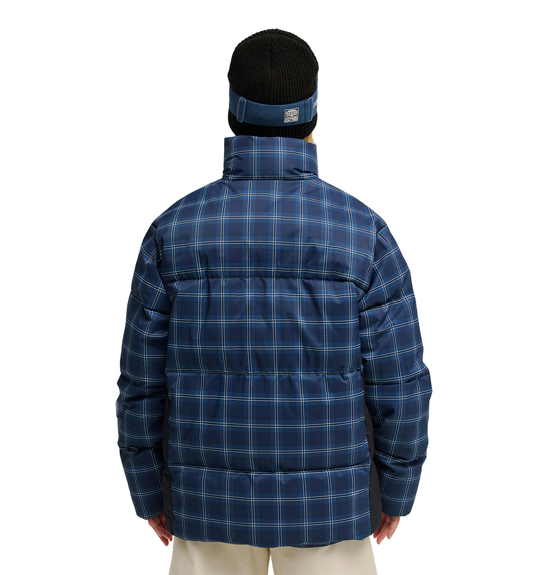 A person is seen from behind, wearing the DC Shoes Trackstar Puffer 10K jacket in blue plaid, paired with cream pants and a black beanie featuring a blue headband. The background is plain white.