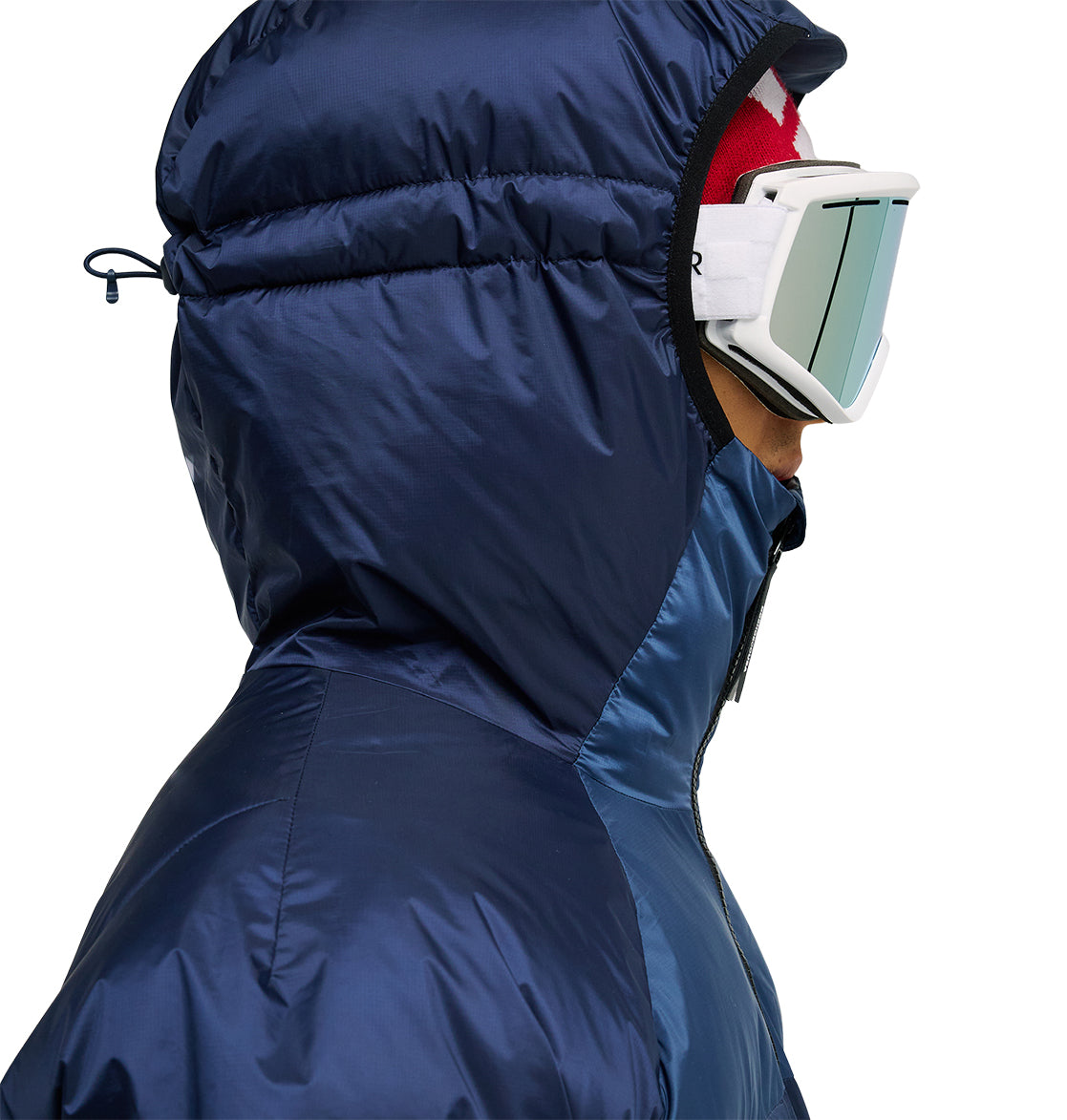 A person shown in side profile against a plain background wears the DC Shoes Powder Puffer 10K, a shiny blue hooded jacket engineered for superior insulation and snow performance, paired with a red hat and large white ski goggles.