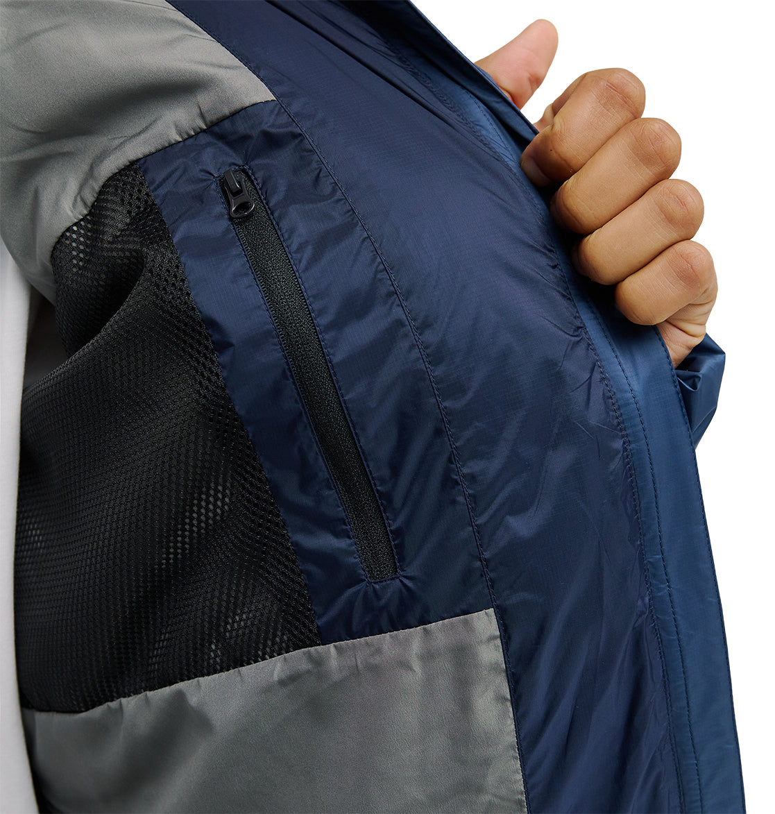 A person holds open the DC Shoes Powder Puffer 10K jacket in blue and gray, revealing a black mesh inner pocket with a vertical zipper—highlighting the jacket’s insulation designed for enhanced snow performance.