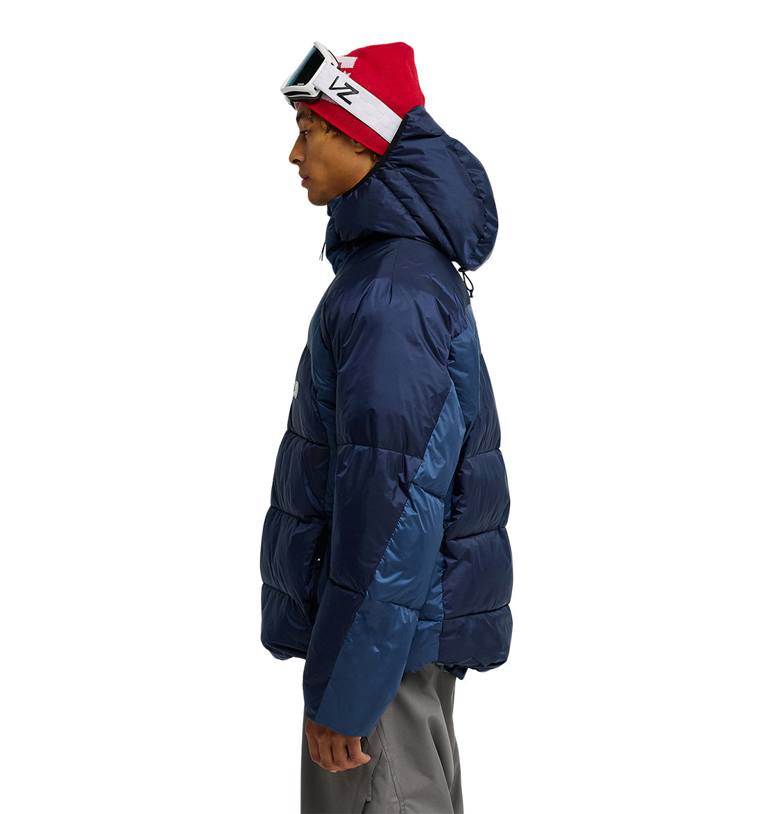A person wearing the DC Shoes Powder Puffer 10K jacket in blue, paired with gray pants and a red beanie with ski goggles, stands in profile facing left against a white background, showcasing the Powder Puffer 10K’s superior insulation and snow performance.