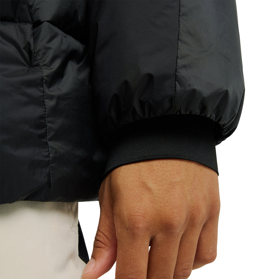 A close-up of a person’s hand and arm wearing the DC Shoes Powder Puffer 10K black jacket with elastic cuffs and light-colored pants, designed for breathable protection.