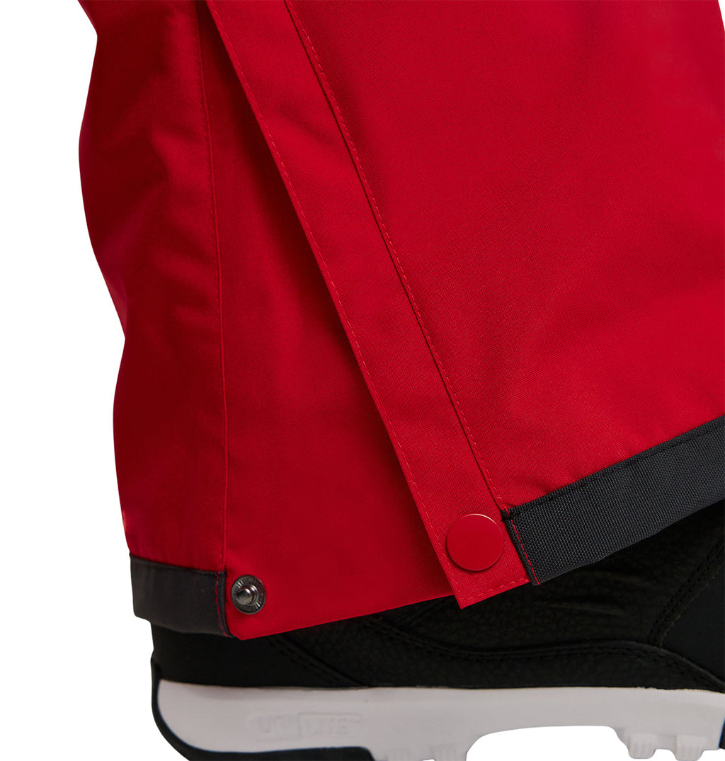 Close-up of the lower leg of a person wearing DC Shoes Banshee Pants in red with snap buttons, paired with black footwear featuring a visible white sole.