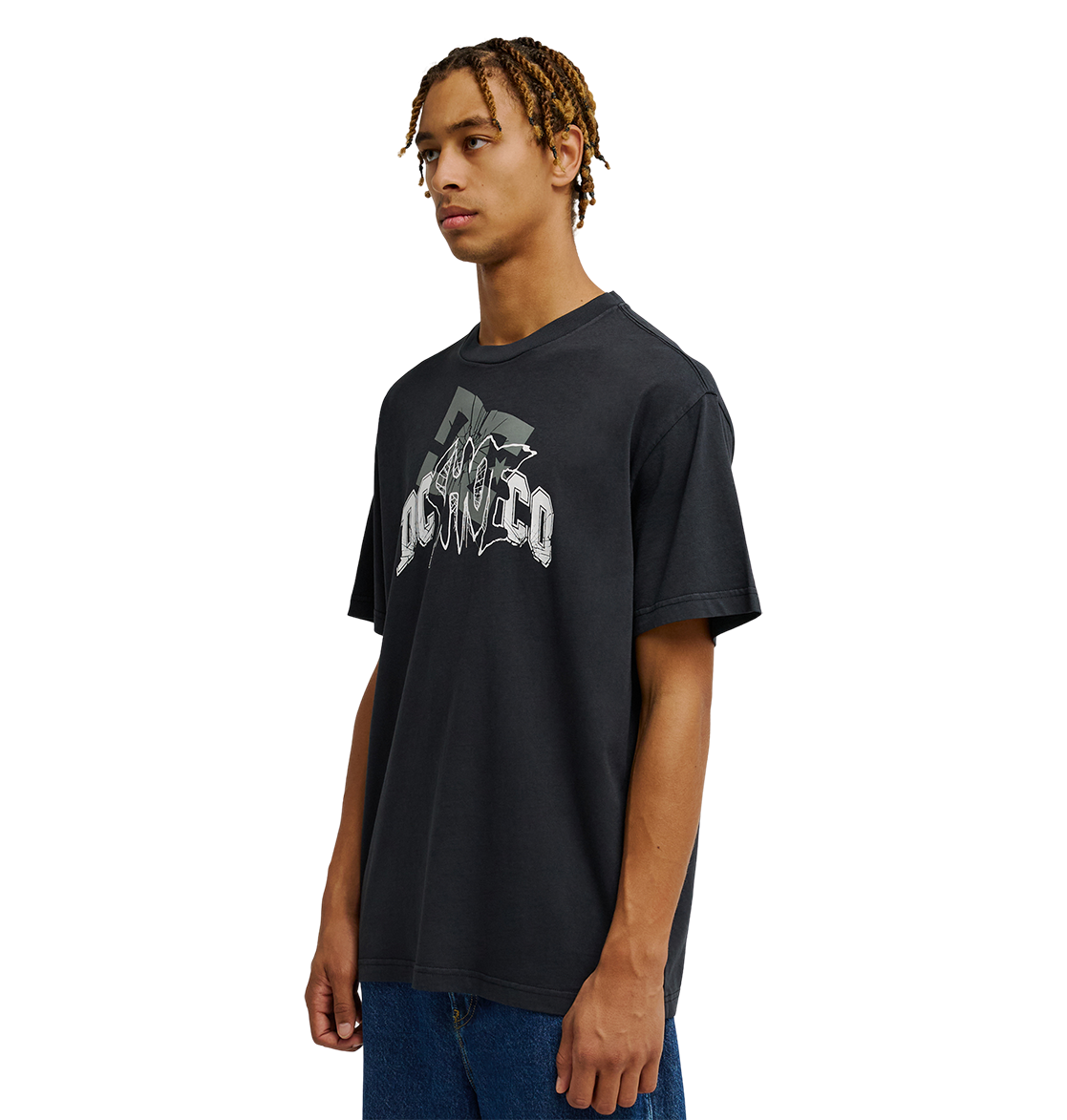A young man with braided hair wears the Men's DC Speratic Tee by DC Shoes—a relaxed fit black graphic skate t-shirt featuring heritage-inspired artwork and stylized text—paired with blue jeans, standing against a plain white background.