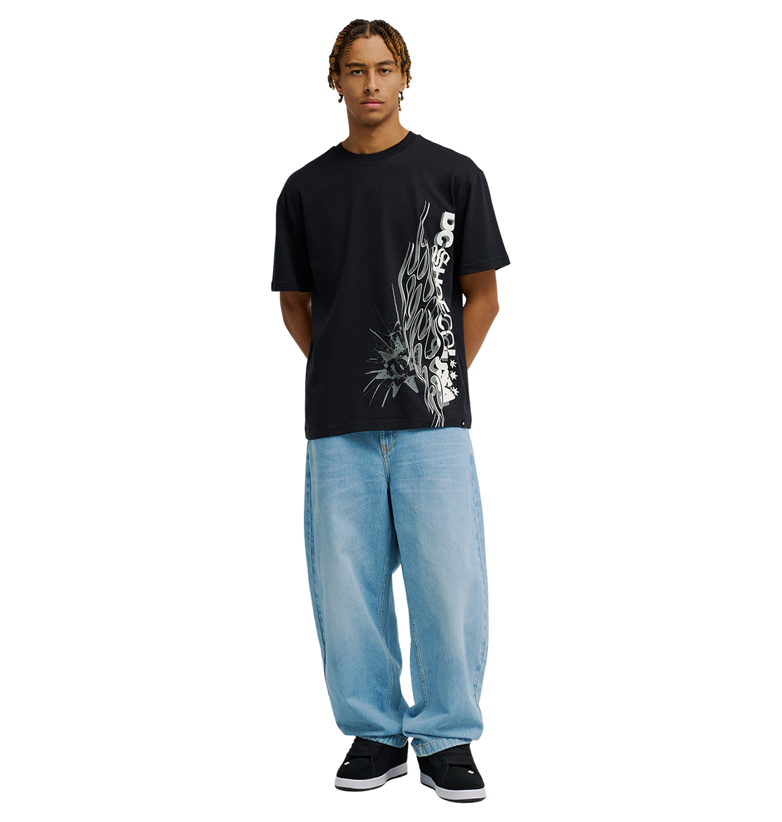 A person stands facing forward, wearing the Men's DC Side Flame Tee by DC Shoes—a black graphic tee with white abstract text and DC artwork-inspired designs—paired with loose light blue jeans and black sneakers, against a plain white background.